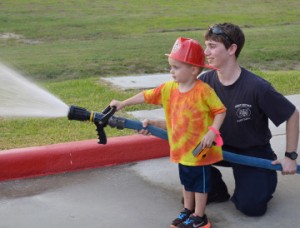 Bryce Brentlinger, 3, of Port Neches, uses afire hose with the assistance of Port Neches Firefighter John Brown during the fire department’s open house on Thursday. Mary Meaux/The News