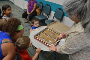 Michael Toon, top, watches as Librarian Molli Hall cuts a piece of cookie cake during an early celebration of National Chocolate Chip Cookie Day at the Marion and Ed Hughes Public Library in Nederland on Wednesday. Mary Meaux/The News